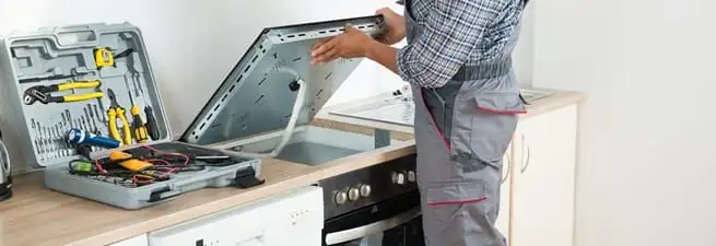 Cooktop repair technician lifting a built-in stovetop for service in Little Rock, AR