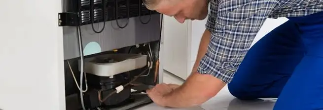 Refrigerator repair technician servicing the compressor and condenser area in Little Rock, AR