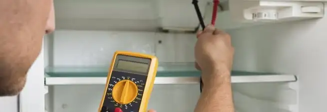 Refrigerator repair technician testing electrical components with a multimeter in Little Rock, AR